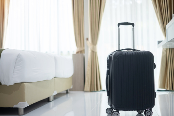 Fekete poggyász a modern szállodai szobában ablakokkal, függönyökkel és ágy háttér. Utazás, kikapcsolódás, utazás, utazás és nyaralás - Fotó, kép