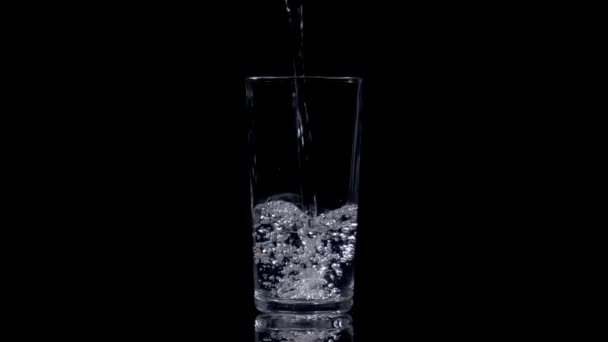 Filling a glass with fresh mineral water on black background. Healthy drinking. Slow motion footage at 180fps. - Felvétel, videó