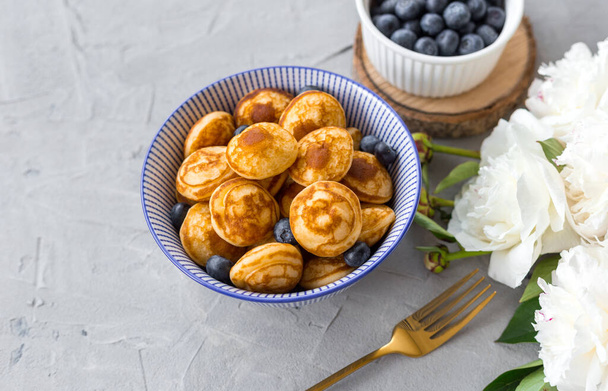 Mini-Müsli-Pfannkuchen mit Blaubeeren in einer Schüssel auf grauem Hintergrund. Trendy Food-Konzept, Frühstückszeit für Kinder. Speisekarte - Foto, Bild