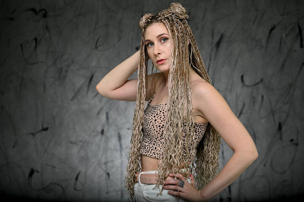Portrait of a caucasian fashionable woman with afro dreadlocks long hair in studio. Pretty model posing on a gray background standing right in front of the camera - Foto, Imagem
