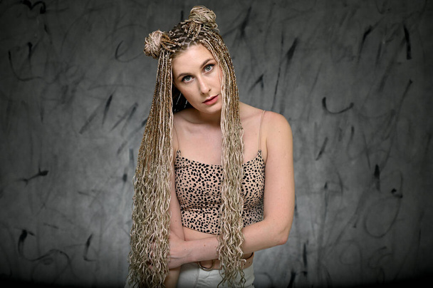 Portrait of a caucasian fashionable woman with afro dreadlocks long hair in studio. Pretty model posing on a gray background standing right in front of the camera - Photo, Image