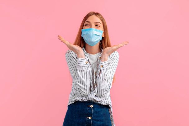 excited, girl in a medical protective mask on her face, looking away, on an isolated pink background - Фото, изображение