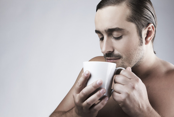 Happy young Caucasian guy having a cup of coffee isolated on gray backgroun - Fotó, kép