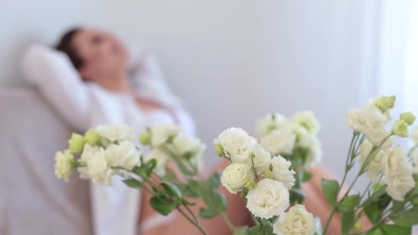 Fiatal nő öltözött fehér fehérnemű és peignoir feküdt az ágyban a hálószobában - Felvétel, videó