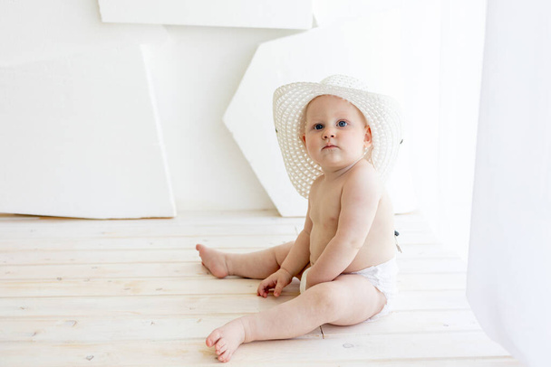 bambino 8 mesi seduto in pannolini con un cappello bianco alla finestra, posto per il testo - Foto, immagini