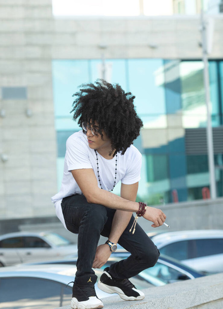 Young black man with curly hair smoking outdoors. - Valokuva, kuva