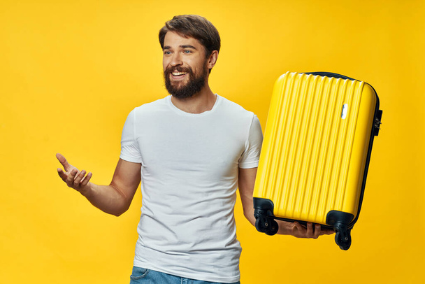 A man in a T-shirt and jeans with a yellow suitcase in his hands laughs - Foto, imagen