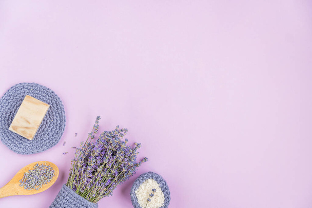 Lavender flowers are arranged on a purple background. cosmetic set with lavender herbs, handmade soap bars and sea salt. Flat lay, copy space - Foto, Imagen