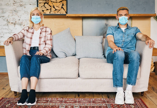 Man and woman in facemask sitting on sofa at home - Photo, image