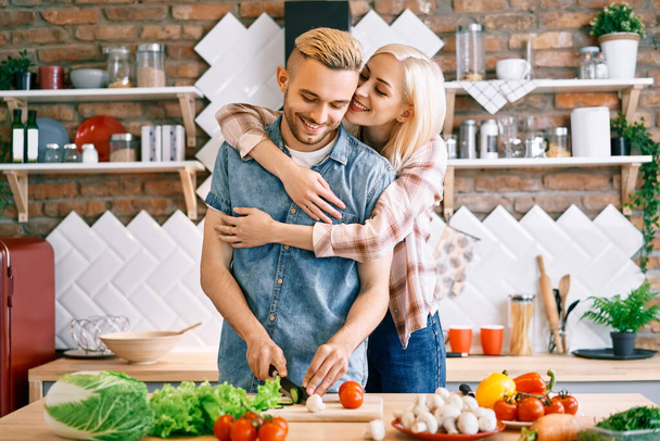 Smiling young couple cooking together vegetarian meal in the kitchen at home. Woman embracing man - Foto, immagini