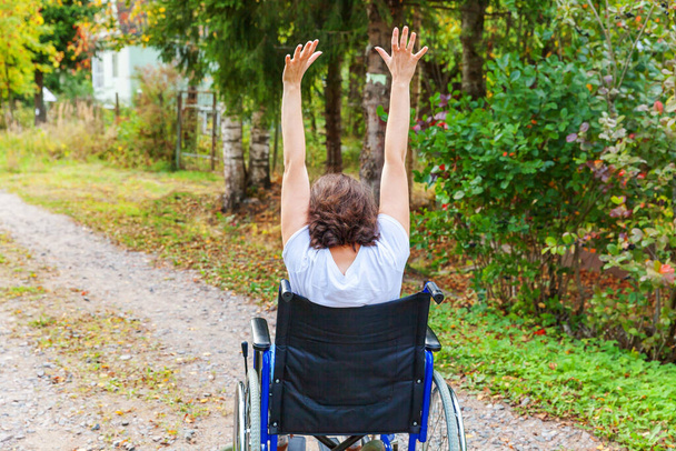 Молода щаслива жінка в інвалідному візку на дорозі в лікарняному парку насолоджується свободою. Паралізована дівчина в некоректному кріслі для людей з обмеженими можливостями на природі. Концепція реабілітації
 - Фото, зображення