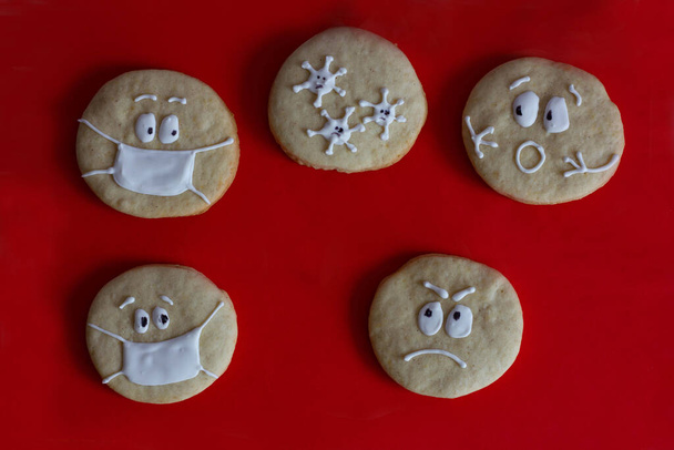 kulaté cukrové sušenky s malovanými tvářemi na červeném pozadí, koronavirus útočí na lidi bez masek, strachu, strachu, maskovaných cookies - Fotografie, Obrázek