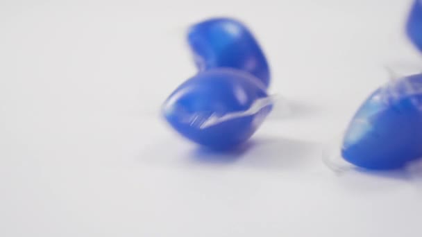 Egy közeli kép egy kék mosogatógép gél hüvelyek alá egy fehér háttér. Háztartási tisztítószerek. Lassú mozgás. - Felvétel, videó