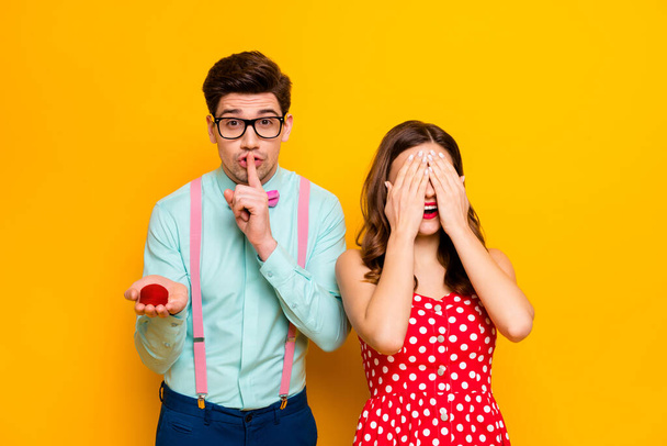 Photo of pretty lady closing eyes handsome guy boyfriend finger on lips hold girlfriend proposal ring box ask keep silence wear red dress shirt bowtie pants isolated yellow color background - Foto, Imagem