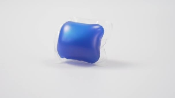 Pod with blue dishwasher gel falls on a white background close-up. Homemade cleaning product. Slow motion - Video