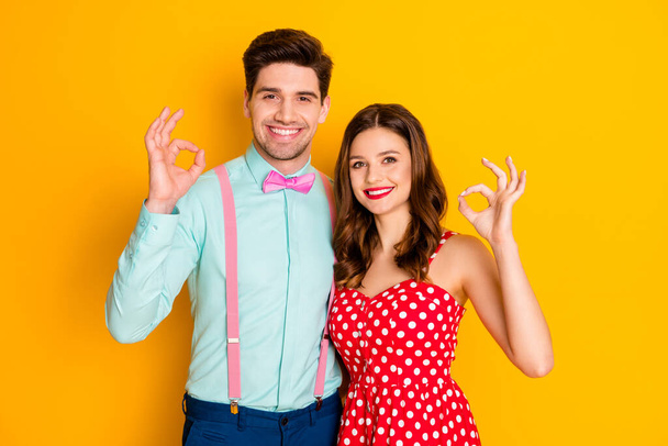 Photo beautiful pretty lady handsome guy toothy smiling prom couple showing okey symbols hands wear red dotted dress shirt bowtie retro clothes isolated yellow bright color background - Φωτογραφία, εικόνα