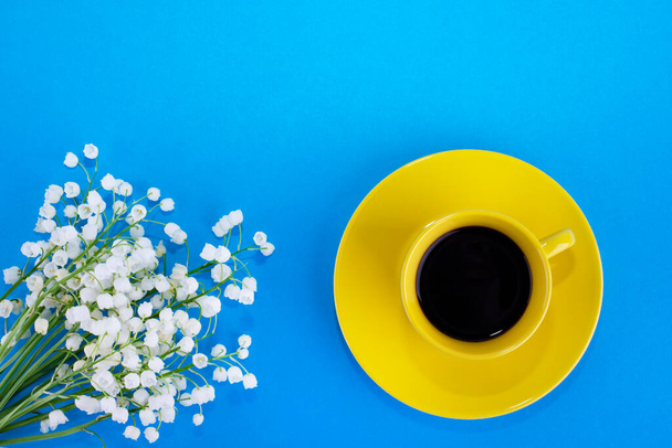 Yellow cup with coffee on a blue background. Lily of the valley flowers - Foto, imagen
