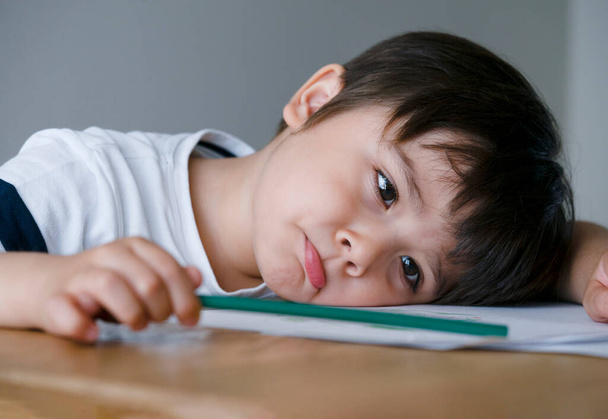 Portret Chłopiec trzymający kolorowy ołówek siedzący samotnie i patrzący z znudzoną twarzą, przedszkolak kładący głowę na stole ze smutną twarzą, Pięcioletni dzieciak znudzony pracą domową w szkole, rozpuszczone dziecko - Zdjęcie, obraz