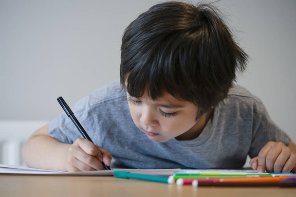 Retrato de um miúdo pré-escolar a fazer trabalhos de casa em casa. Criança feliz desenho com lápis coloridos, menino está escrevendo na mesa, escola primária e conceito de educação
 - Foto, Imagem