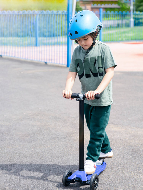 Portrait boy learning to ride a scooter in playground in sunny day summer, Prortrait Child in safety helmet riding a roller, Kid playing outdoors, Active leisure and outdoor sport for children. - Valokuva, kuva