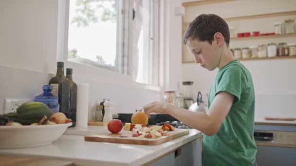 Young boy working in the kitchen slicing fruit for breakfast - Materiał filmowy, wideo