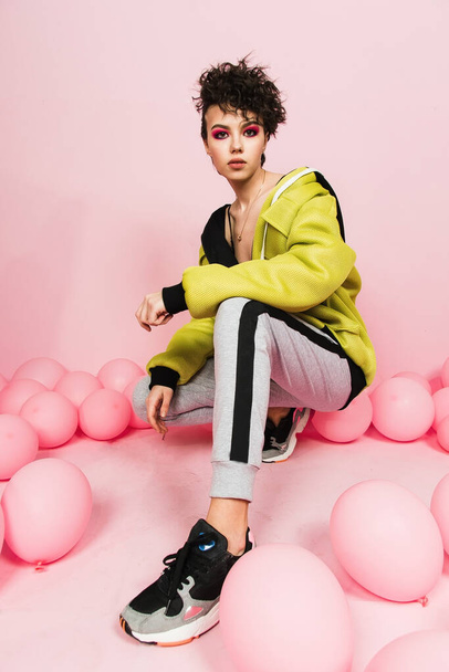 A young girl in a tracksuit in a pink studio on the background of small balloons. Sport and holiday concept. - Fotografie, Obrázek