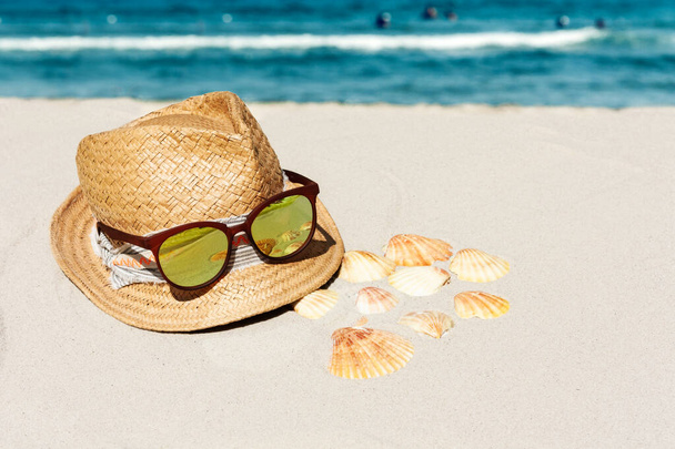 Vintage summer wicker straw beach hat and sunglasses on the beach near the sea - Foto, afbeelding