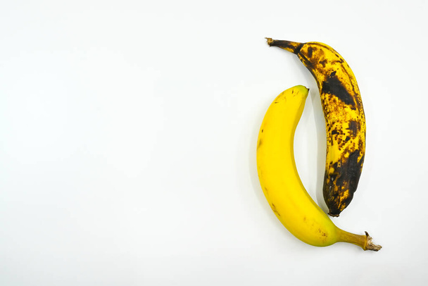 Dva banány vedle sebe na bílém pozadí. Jeden je zralý a druhý hnije. Žádní lidé. Mezera pro kopírování vlevo. - Fotografie, Obrázek