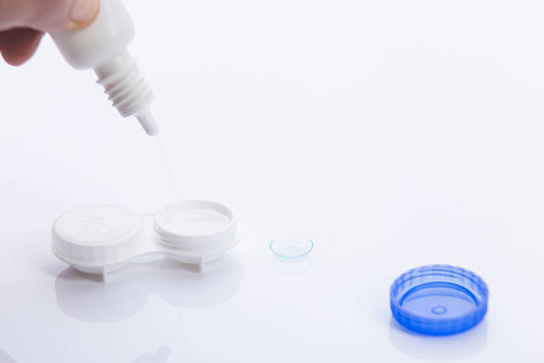 hand adding solution in contact lenses case on white background. - 写真・画像