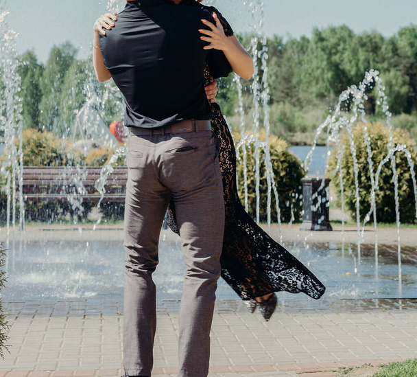 young couple woman in a long elegant lace black dress man in trousers and shirt. love story outdoors, tenderness, hugs - Fotó, kép