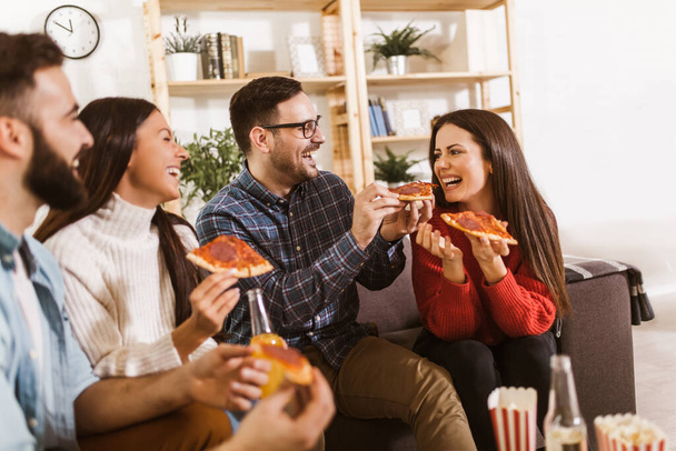 Egy csapat fiatal barát pizzát eszik otthon. A fiatalok jól érzik magukat együtt.  - Fotó, kép