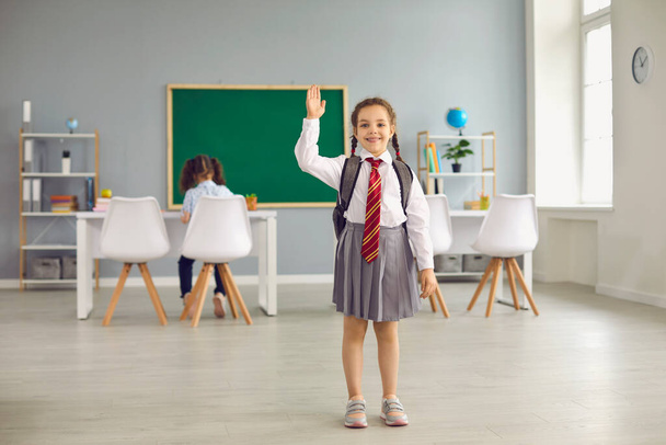 Back to school. Little schoolgirl in uniform raised hands up standing in class. - Photo, Image