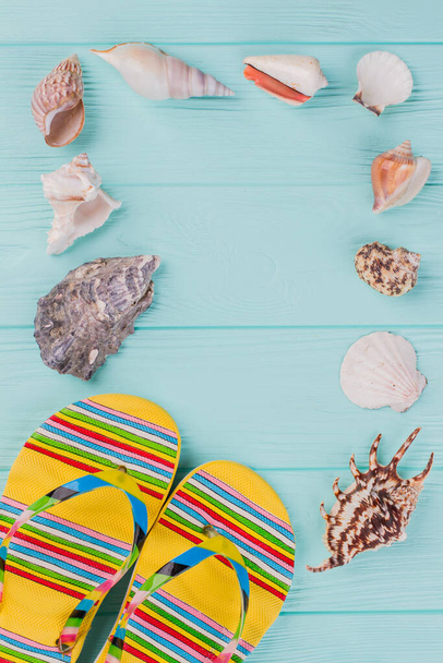 Along the perimeter are different sea shells and bright sandals in the corner on turquoise background. - Foto, Imagen