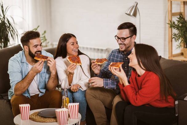 Grupo de jóvenes amigos comiendo pizza en el interior del hogar. Jóvenes divirtiéndose juntos
.  - Foto, imagen