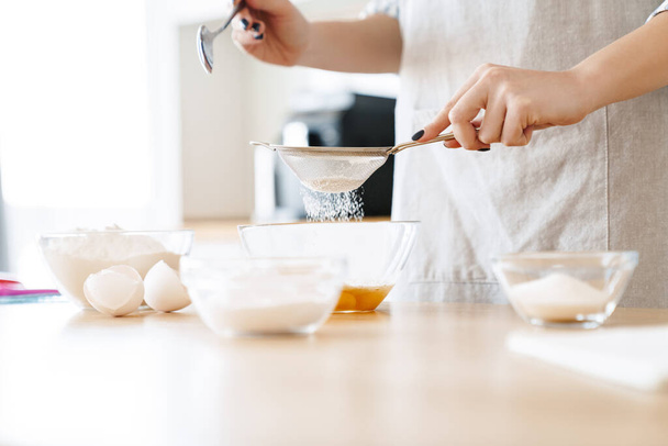 Cropped image of caucasian young woman preparing dough while cooking pie in modern kitchen - Foto, Bild