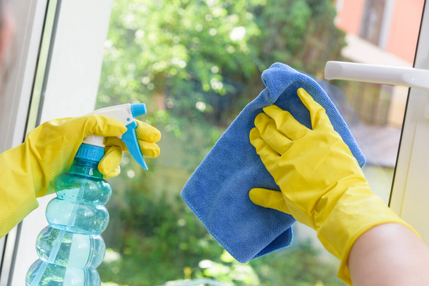 Zárt vinil műanyag ablak tisztítása. Védőkesztyű a kézen és tisztítókesztyű locsolóval - Fotó, kép