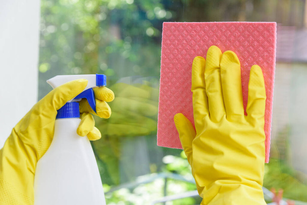 Cleaning of closed vinyl plastic window. Protective yellow gloves on hands and cleaning cloth with sprinkle - Fotó, kép