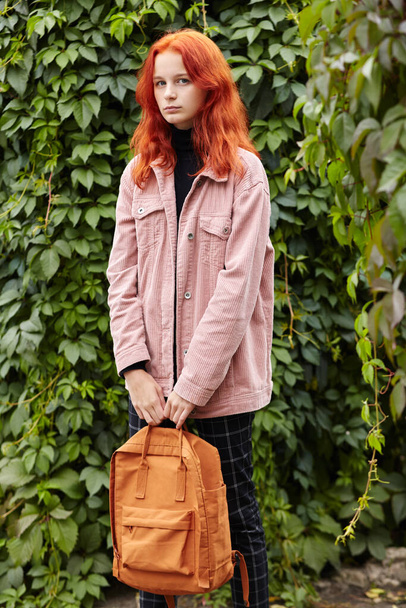 outdoor portrait of a teenage stylish girl with backpack on background of ivy. - Valokuva, kuva