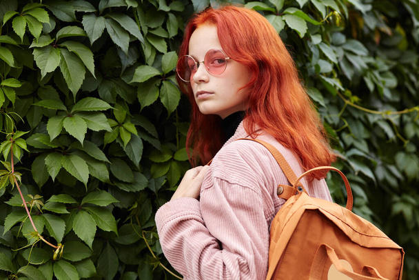 outdoor portrait of a teenage stylish girl with backpack on background of ivy. - Φωτογραφία, εικόνα