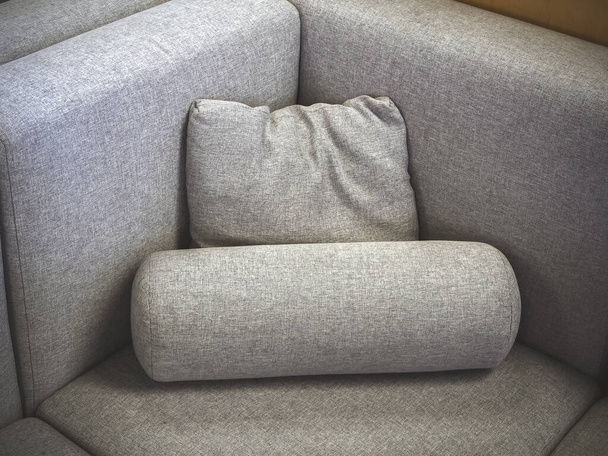 A closeup photo of a fragment of a soft gray fabric sofa with a square and cylindrical pillow. Corner view - Zdjęcie, obraz
