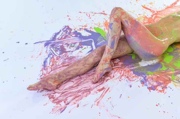 Nude woman in stains of paint on a white floor. View from above. Cropped. Color splashes on the skin. Art body painting. - Foto, Imagem