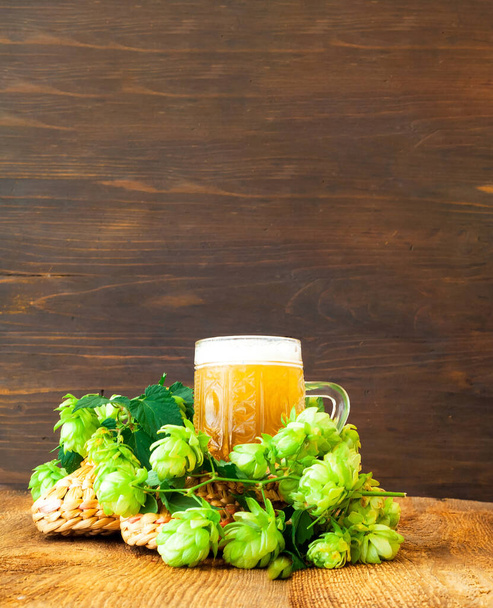 木製の背景にビールと新鮮なホップのマグカップ。国際ビールの日。閉鎖、コピースペース - 写真・画像