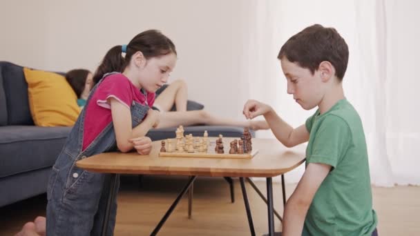 Młode dzieci grające w szachy na stole w salonie - Materiał filmowy, wideo