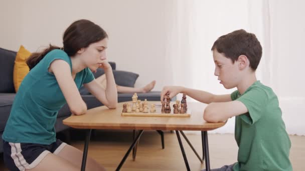 Młode dzieci grające w szachy na stole w salonie - Materiał filmowy, wideo