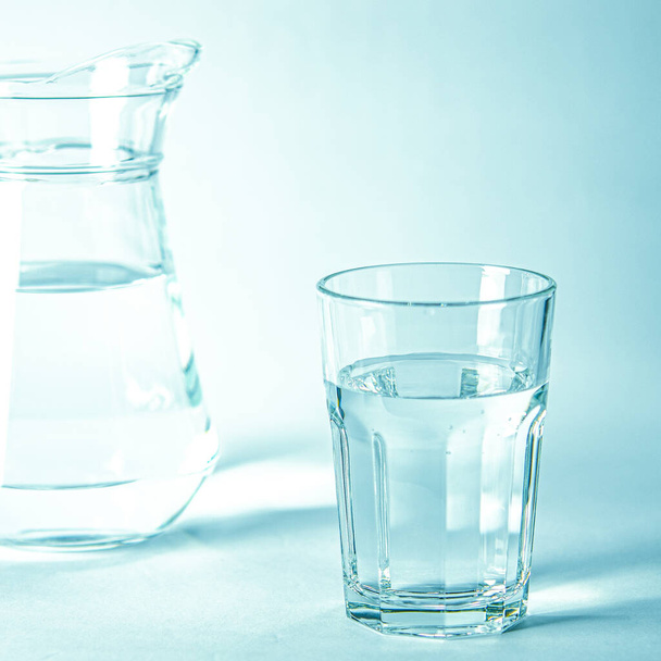 澄んだ水が澄んだガラスは、水のあるクーシュマの隣の青の背景にあります。 - 写真・画像