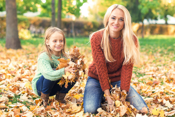 Happy young caucasian mother and little child playing with leaves in nature autumn park - Фото, изображение