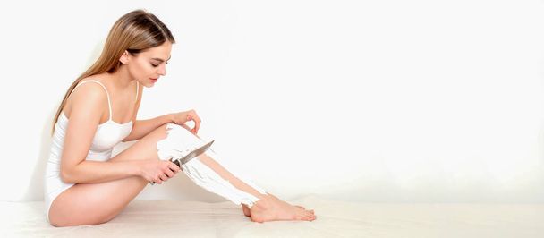 Beautiful young caucasian woman shaves her legs with a knife on a white background - Photo, Image