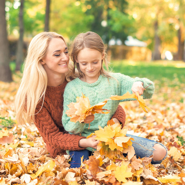 幸せな若いです白人の母親と小さな娘を保持秋の黄色の葉が公園に座って - 写真・画像