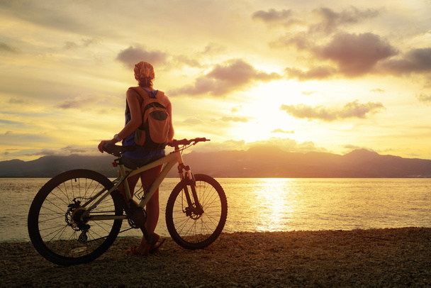 νεαρή γυναίκα με σακίδιο στέκεται στην ακτή κοντά το ποδήλατο - Φωτογραφία, εικόνα