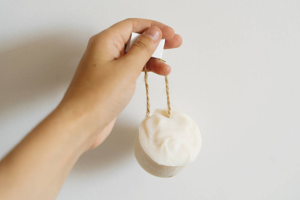 Hand holding solid shampoo bar, natural herbal soap or laundry soap on background of white wall. Plastic free hygiene items. Zero waste bathroom. - Photo, Image